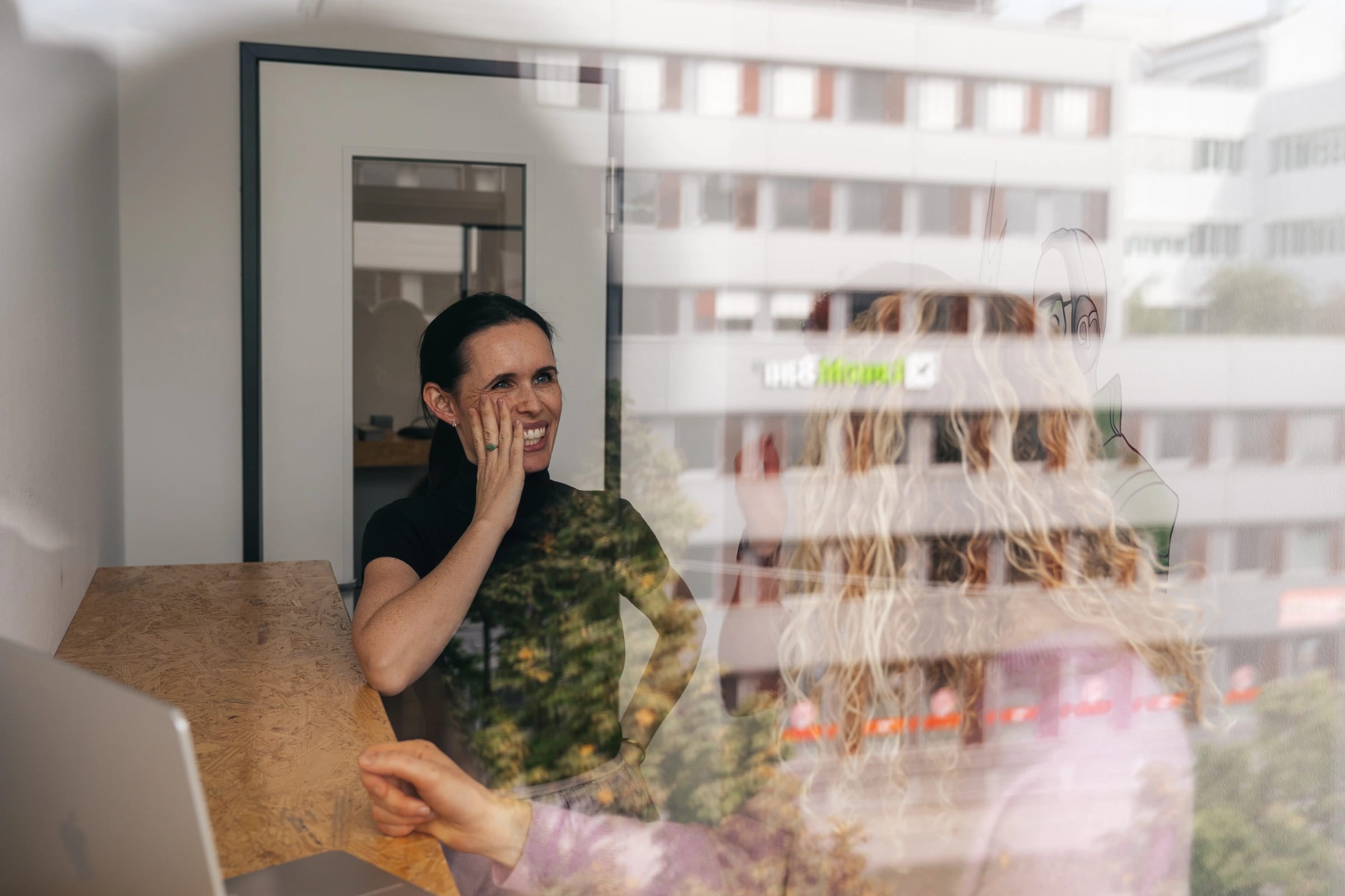 Jessica steht in einem kleinen Besprechungsraum, im Vordergrund spiegelt sich das gegenüberliegende Gebäude.