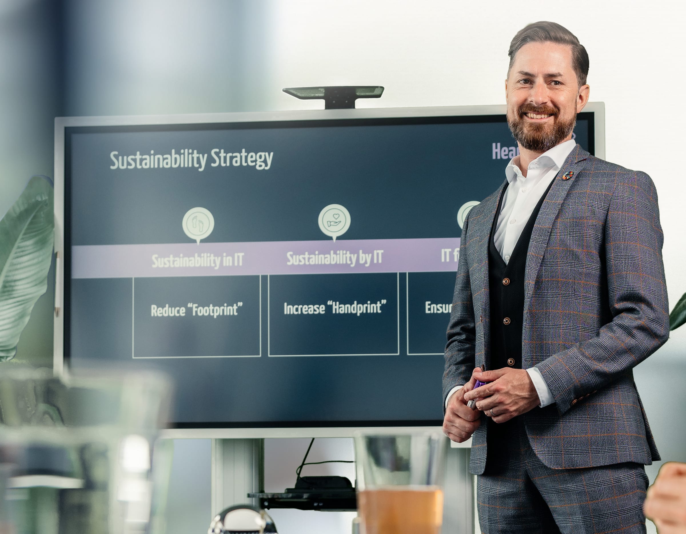 Rainer Karcher steht lächelnd neben einem Bildschirm mit der Präsentation „Sustainability Strategy“