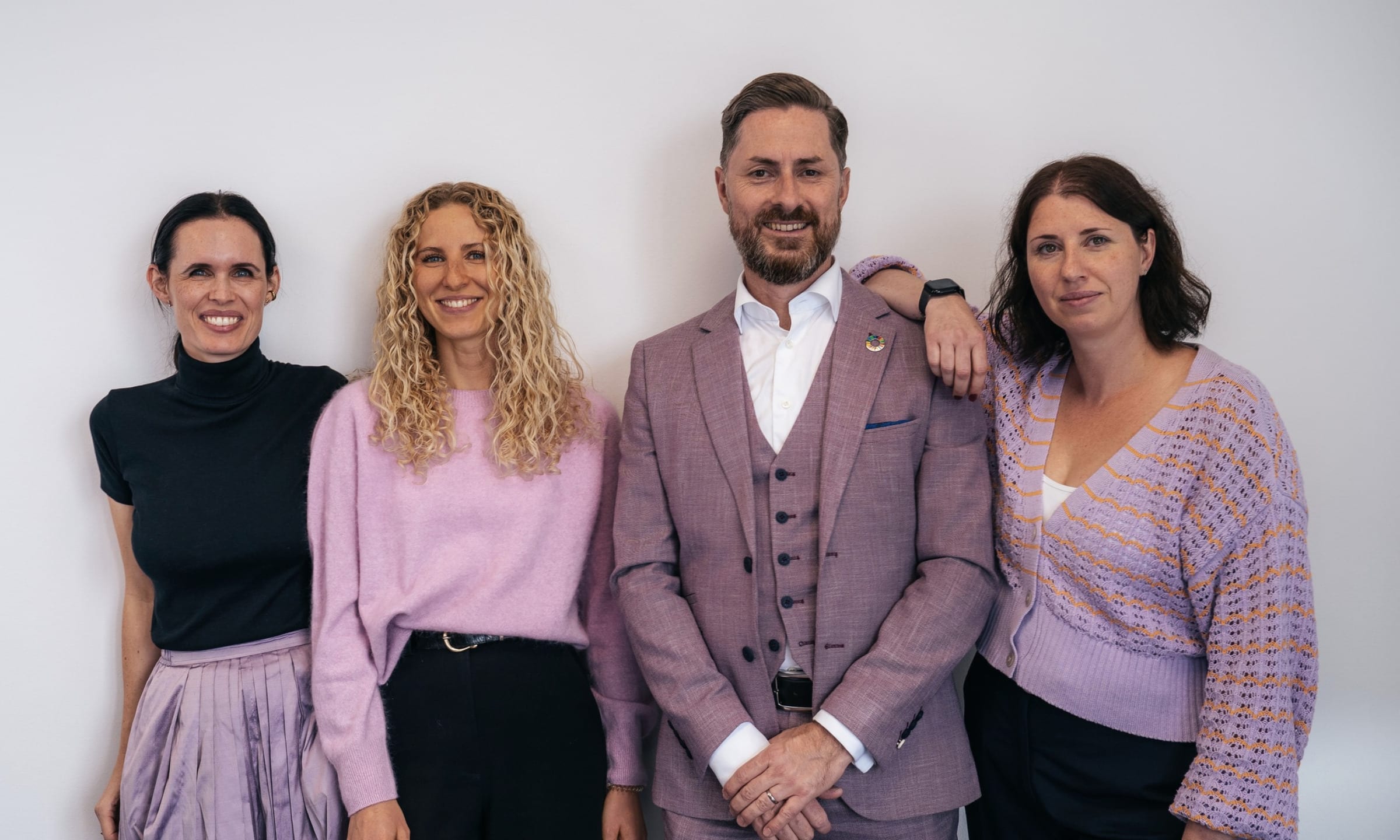 Das Heartprint-Team vor einer hellen Wand: Jessica Ryan-Tietz, Anthea Wagner, Rainer Karcher und Stefanie Karcher, alle in Lila- und Schwarztönen