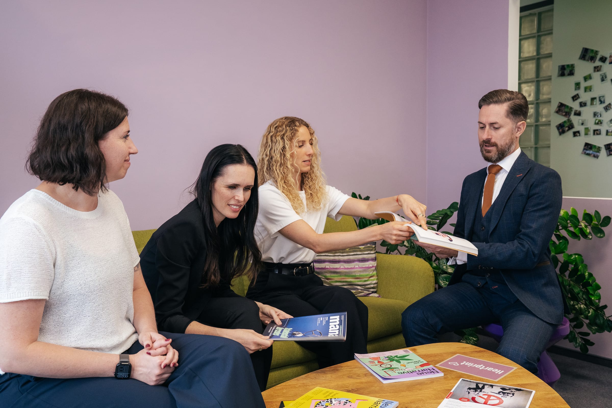 Das Team auf dem Sofa: Anthea Wagner reicht Rainer Karcher ein Magazin, daneben sitzen Stefanie Karcher und Jessica Ryan-Tietz, auf dem Tisch liegen weitere Magazine
